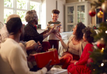 Multi-Generation Family Exchanging And Opening Gifts Around Christmas Tree At Home