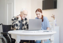 Woman helping disabled elderly man on laptop