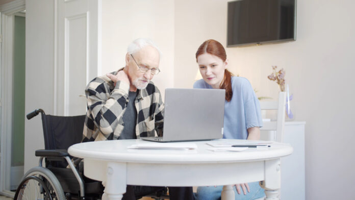 Woman helping disabled elderly man on laptop