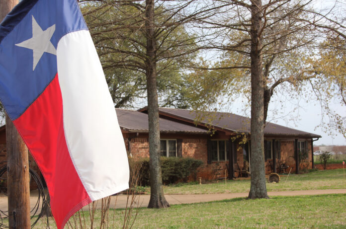 Texas Flag With Brick Ranch House in Background