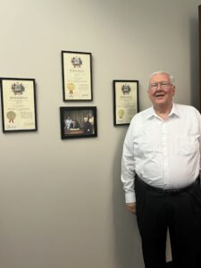 Attorney Robert Morris standing next to his accolades framed on a wall. 