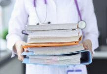 Doctor is holding large stack of folders.