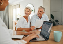 Retirement, savings and couple planning finance, insurance and investments in living room. Man and woman and seniors communication, talking and discuss wealth with internet banking and laptop at home