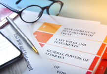 A ballpoint pen and a smart phone rest on top of living trust documents. A pair of eyeglasses sit out of focus in the background.