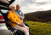 Senior couple sitting against the car, resting after hiking in countryside.