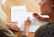Female Friend Helping Senior Woman To Complete Last Will And Testament At Home