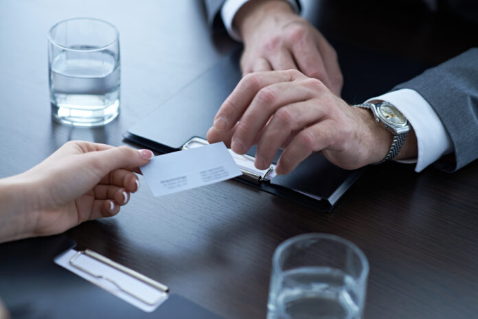 Hand of woman giving business card to businessman