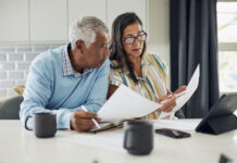 An older couple is sitting at their kitchen table reviewing financial documents.