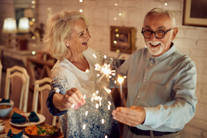 Happy mature couple using sparklers and having fun together on Christmas day at home.